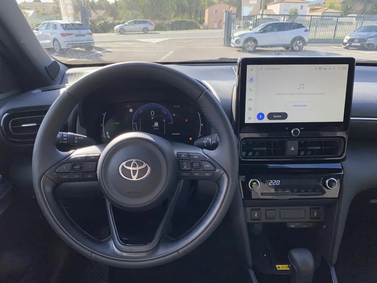 Vue intérieure centrée sur le volant cuir et l'écran tactile du tableau de bord de la Toyota Yaris Cross blanche.