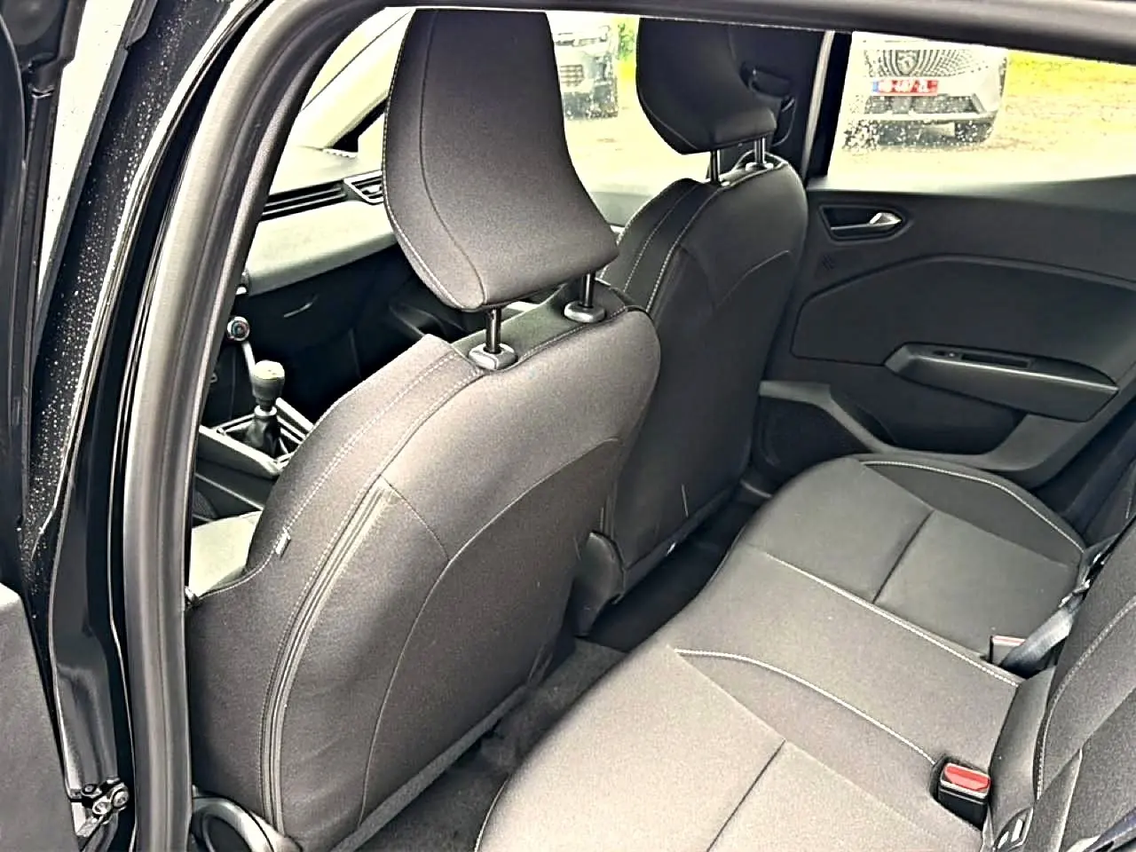 Vue intérieure arrière côté gauche de la Renault Clio V noire, montrant les sièges et la console centrale avec levier de vitesse.