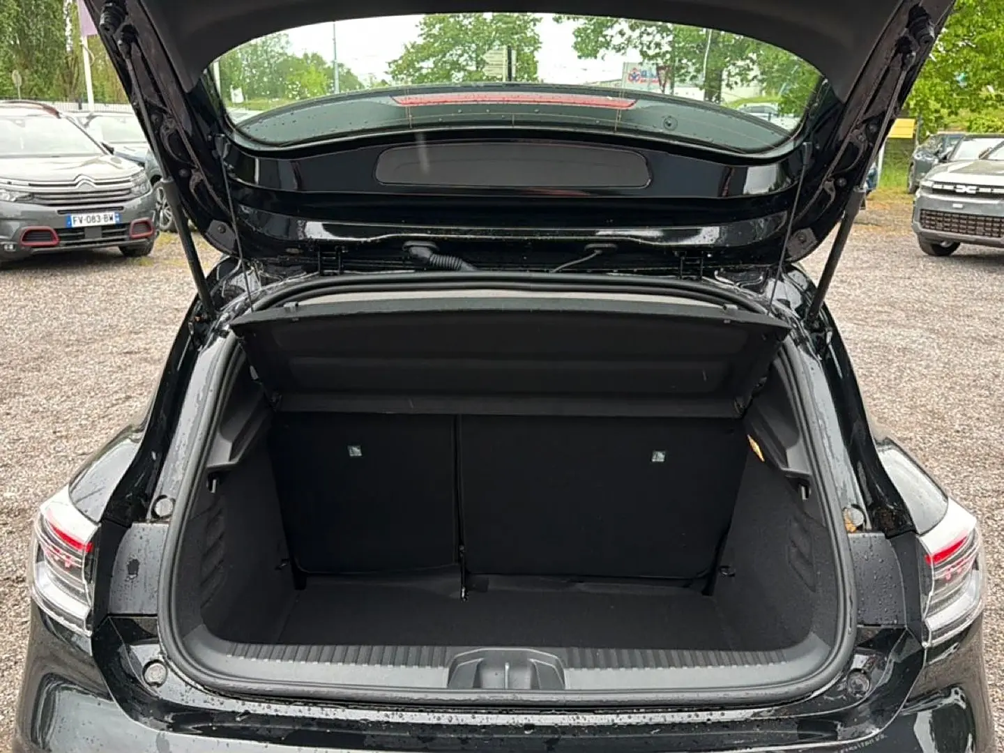 Coffre ouvert vu de l'arrière d'une Renault Clio V noire, montrant l'espace de chargement et les feux arrière LED.