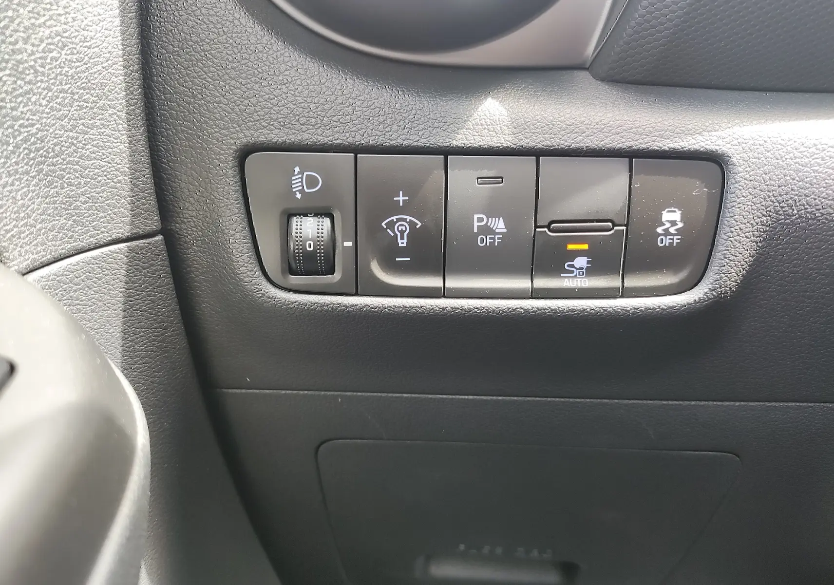 Gros plan sur les commandes de réglage des feux et aides à la conduite dans l'habitacle noir d'une Hyundai Kona Electric 2025.