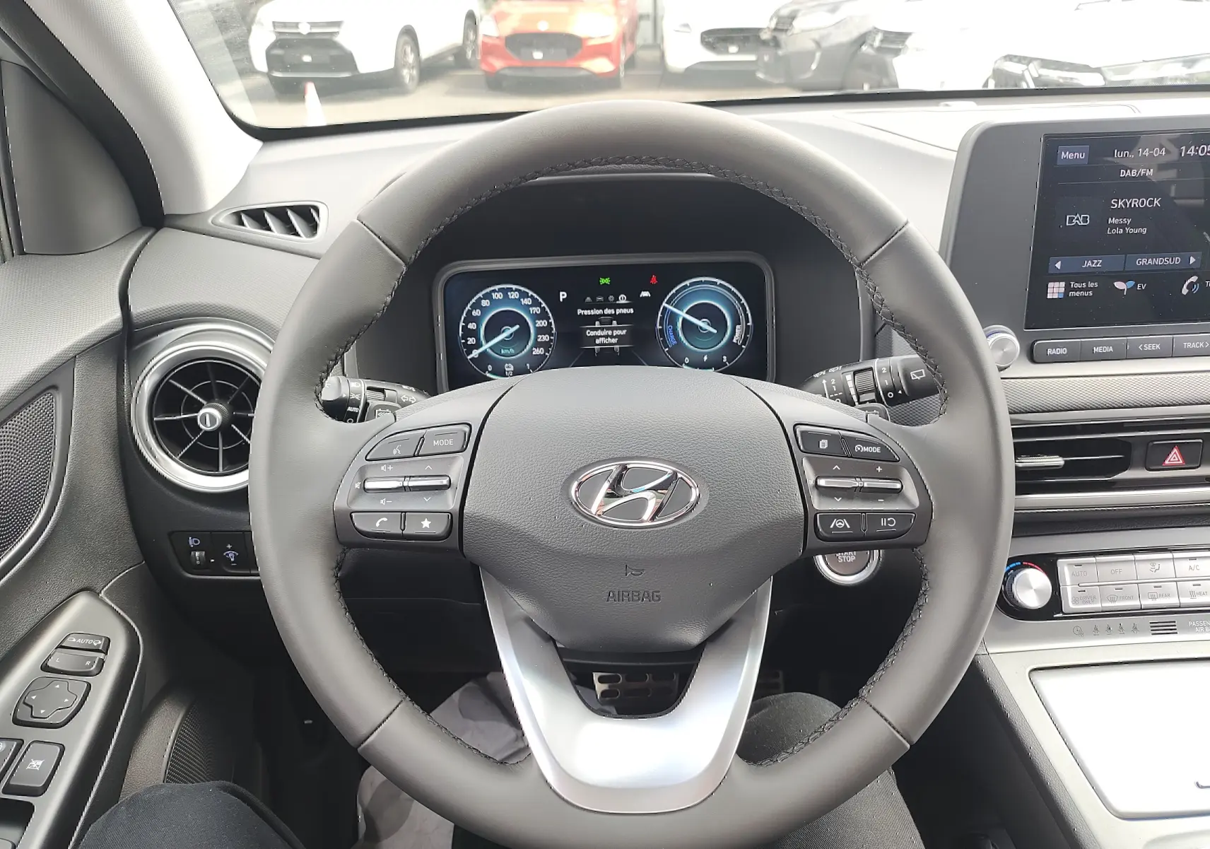 Vue intérieure centrée sur le volant cuir gris du Hyundai Kona Electric 2025 avec tableau de bord numérique et écran tactile.