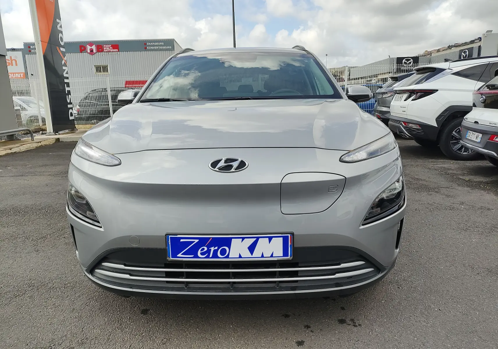 Vue frontale d'un Hyundai Kona électrique gris métallisé avec plaque d'immatriculation Zéro KM visible.