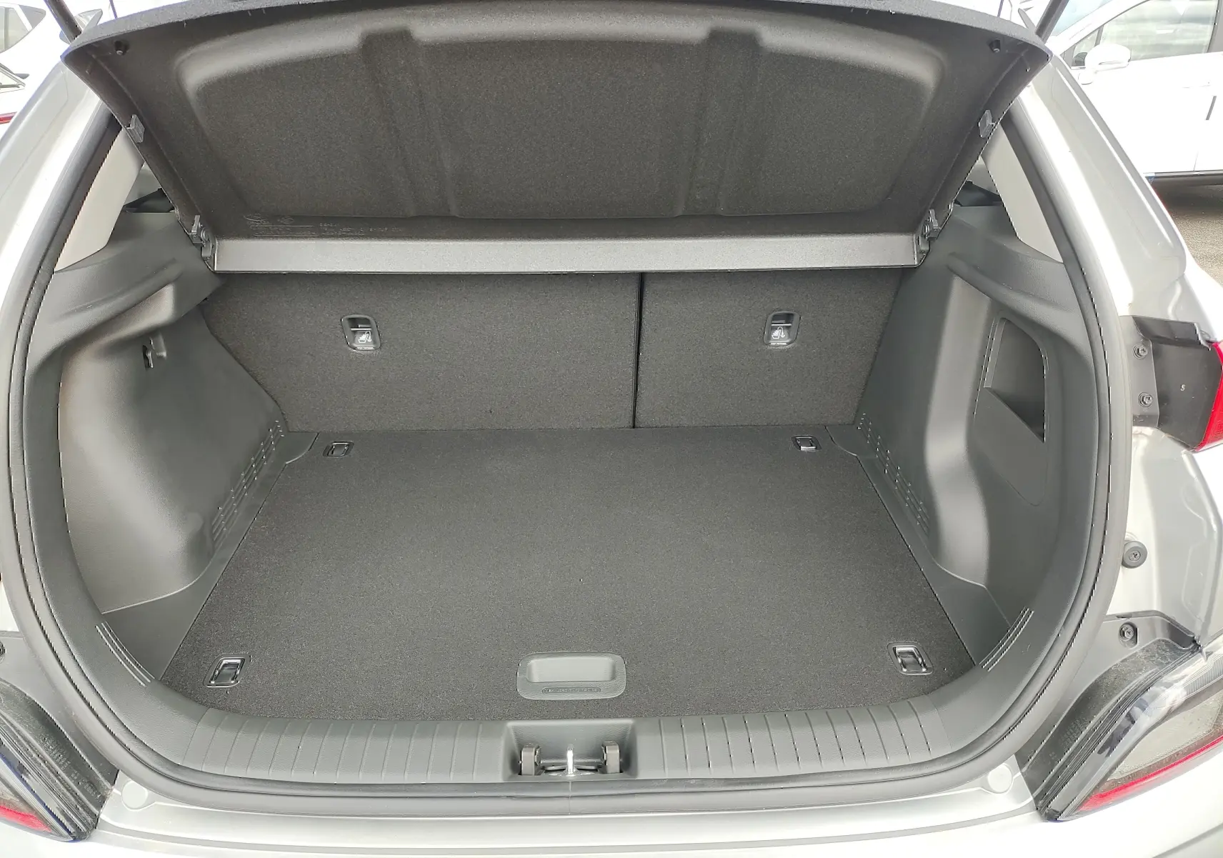 Coffre ouvert d'une Hyundai Kona électrique gris métallisé, vue arrière montrant l'espace de chargement vide.