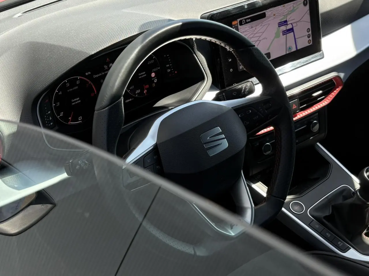 Vue intérieure du volant et tableau de bord numérique d'une SEAT Arona TSI 110 FR avec détails rouges et écran de navigation.