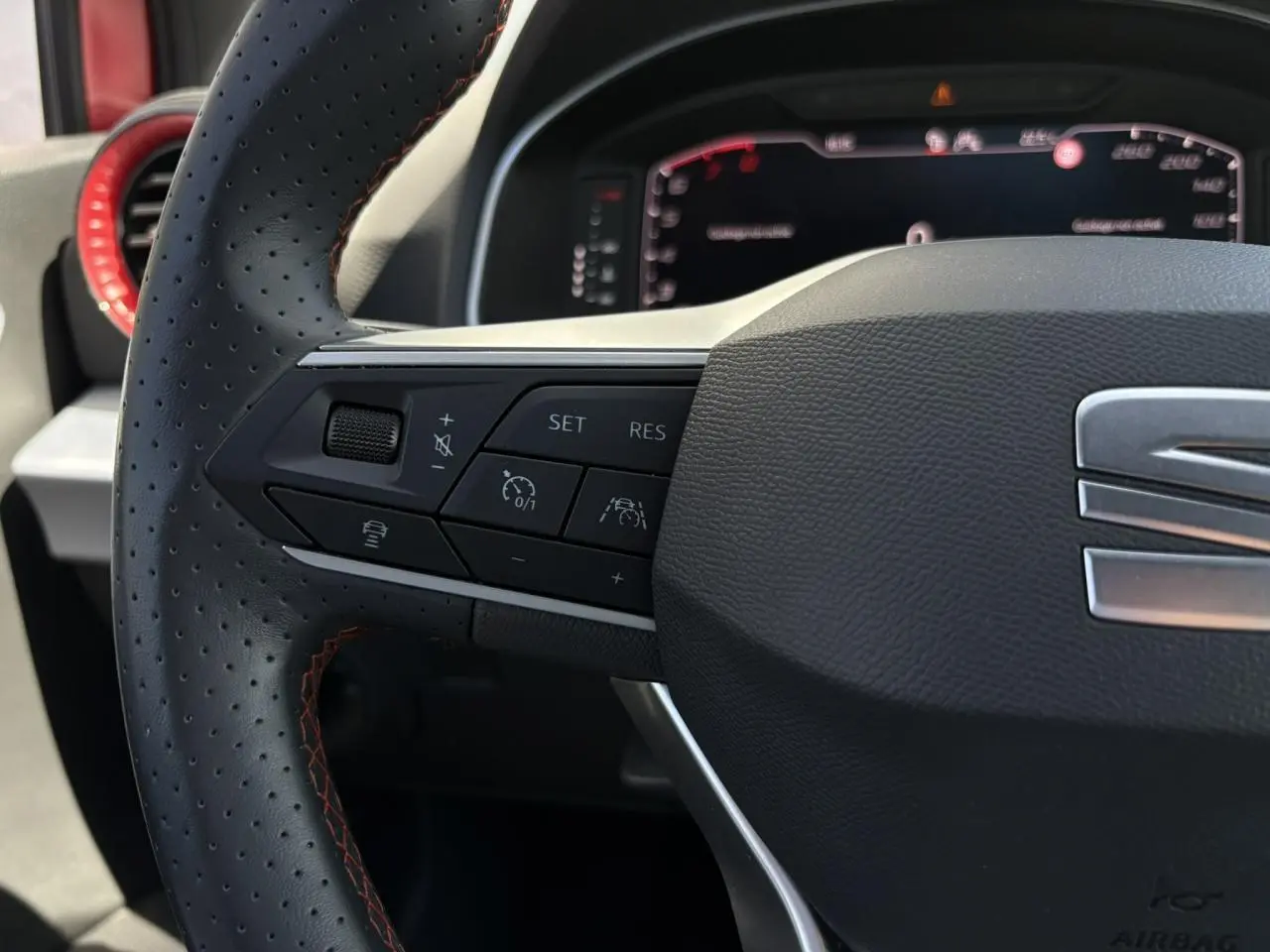 Gros plan sur le volant perforé avec surpiqûres rouges du SEAT Arona TSI 110 FR, boutons de régulateur adaptatif visibles.