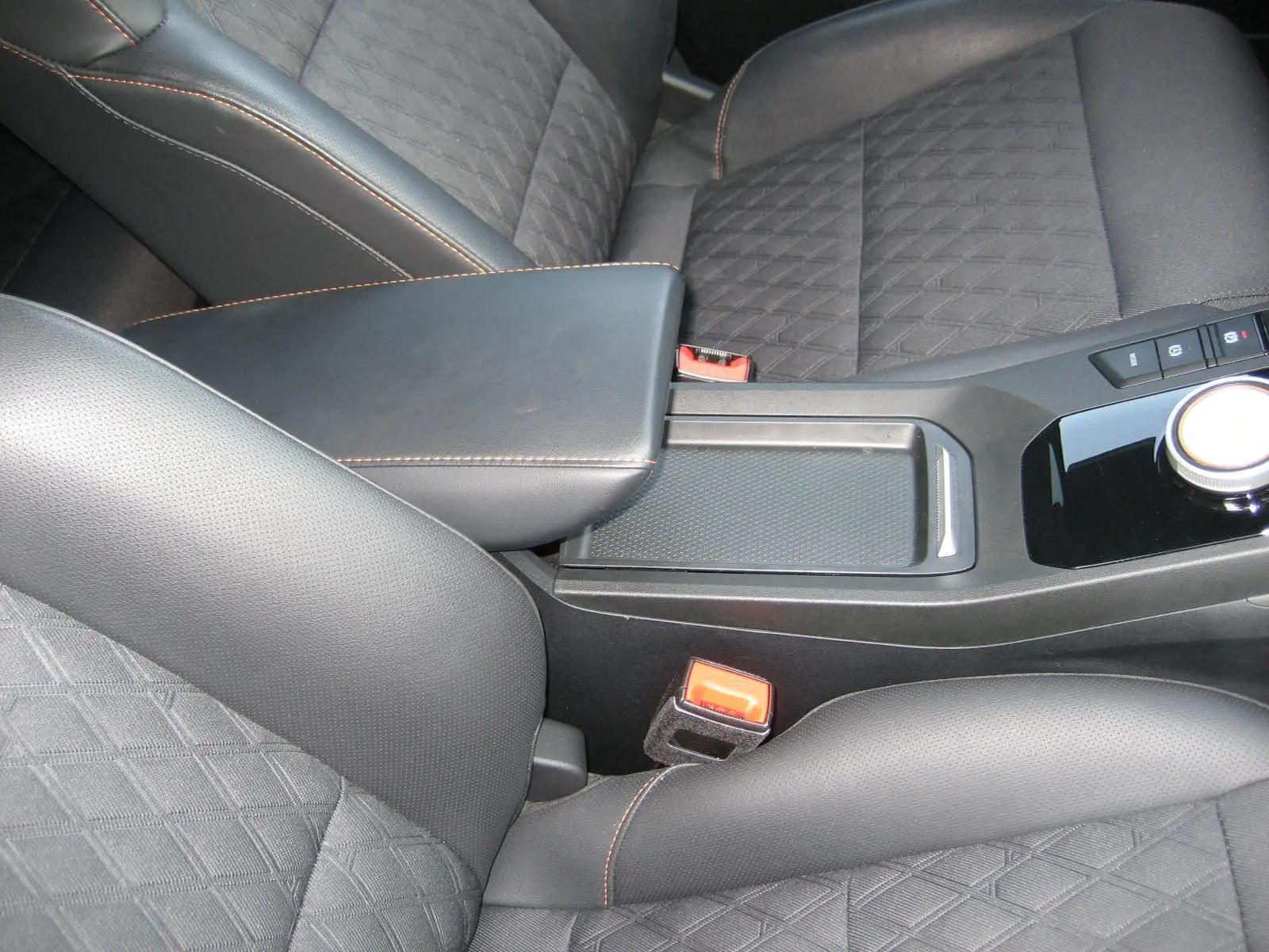 Gros plan sur l'accoudoir central noir et les sièges en cuir noir avec surpiqûres orange du MG3 1.5 HYBRID+ 2024.