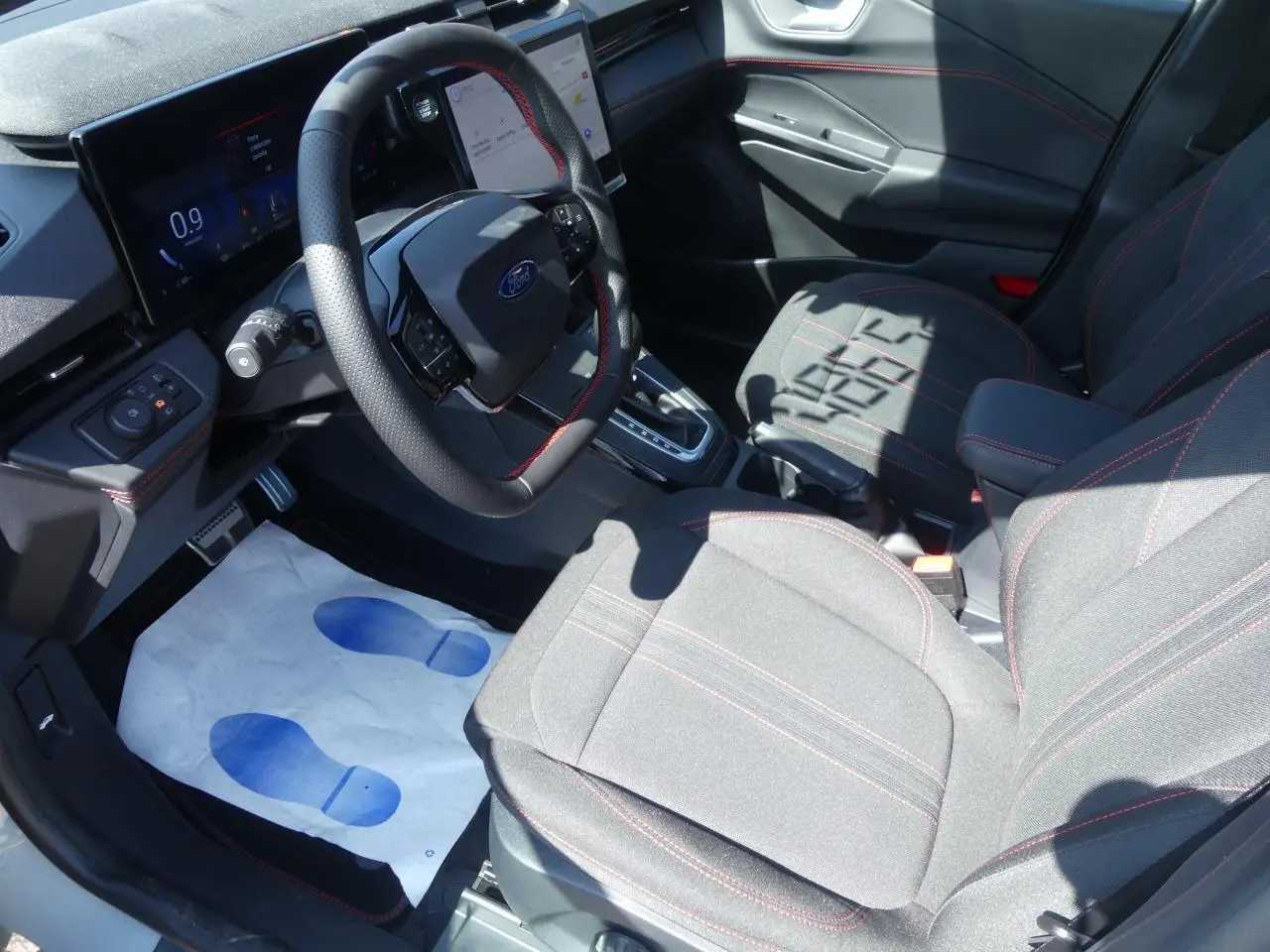 Intérieur avant droit du Ford Puma 2025 avec sièges tissu gris et surpiqûres rouges, volant multifonction et écran digital.