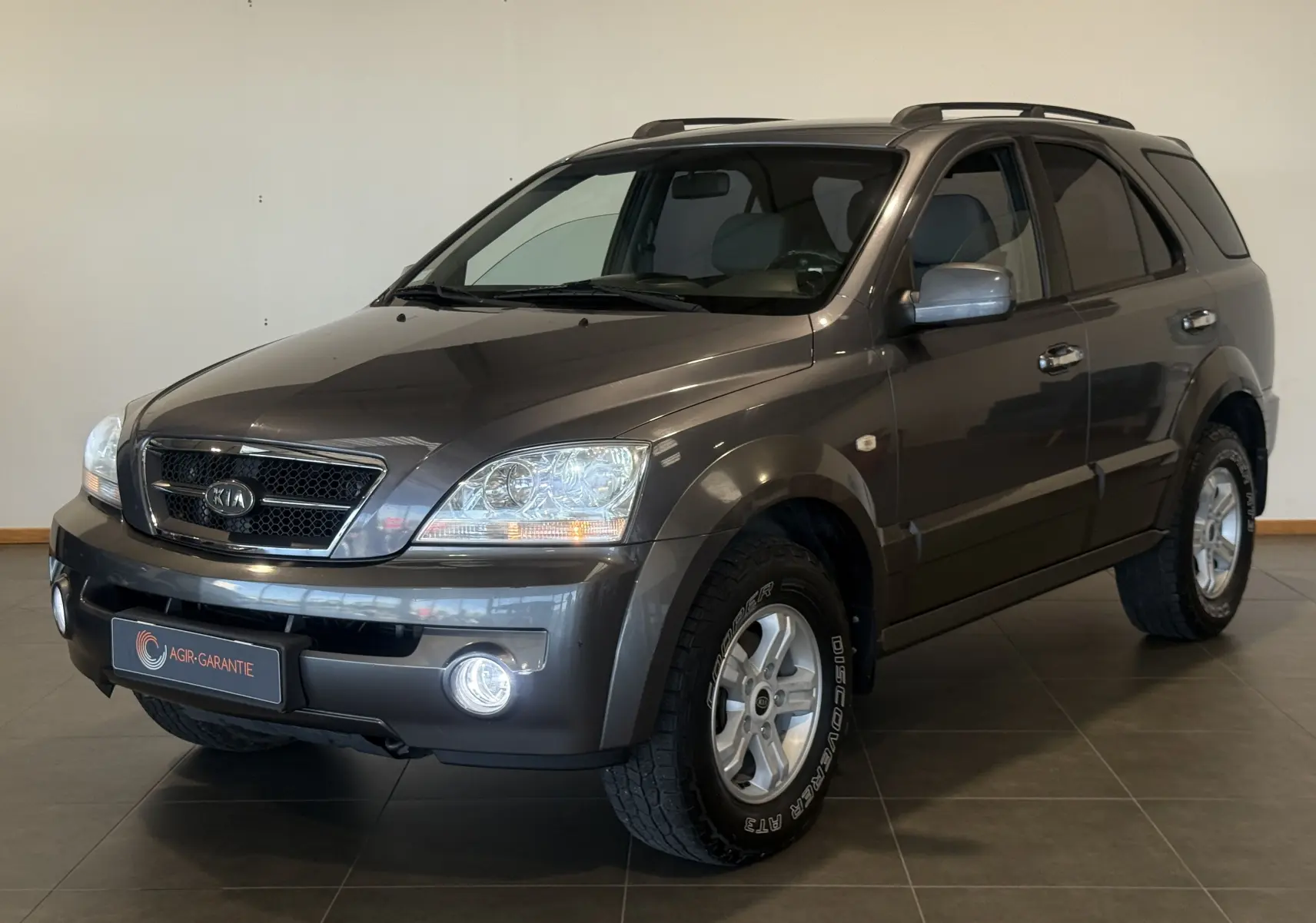 KIA Sorento gris 2005 en 3/4 avant droit, SUV diesel avec phares allumés et jantes alliage visibles.