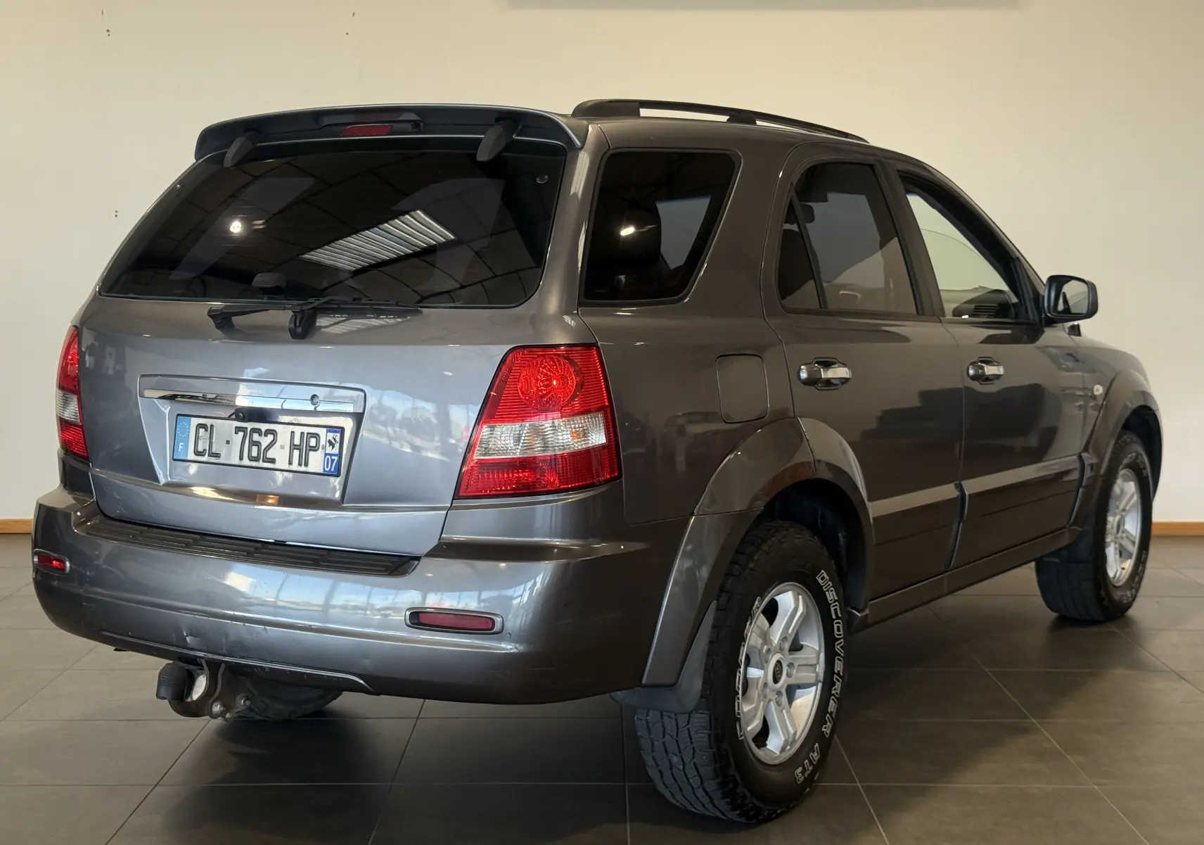 Vue 3/4 arrière droite d'un KIA Sorento gris 2005 avec attelage et pneus tout-terrain visibles.