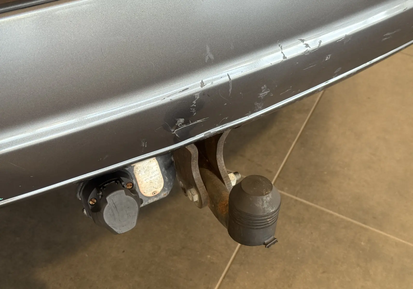 Gros plan sur l'attelage d'une KIA Sorento gris 2005, montrant le crochet de remorquage et la prise électrique arrière.