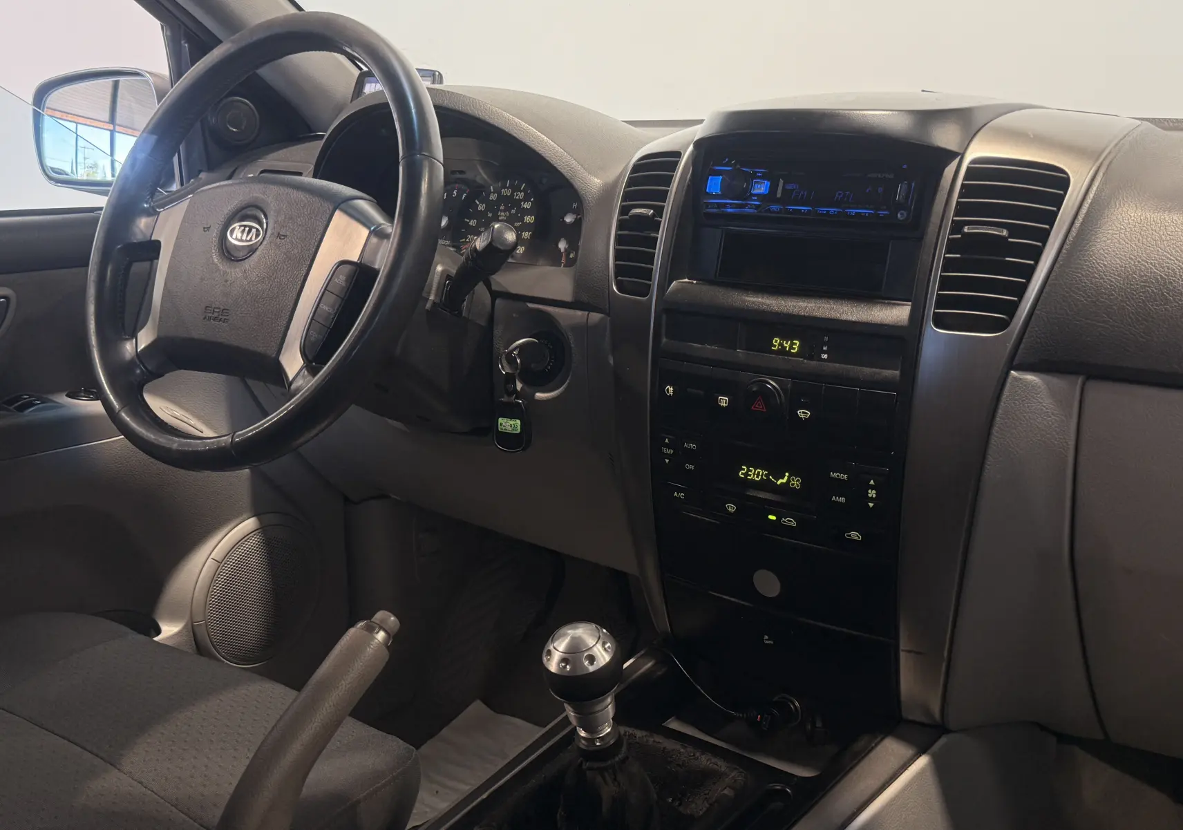Intérieur du Kia Sorento 2005 gris, vue du poste de conduite avec volant, tableau de bord et levier de vitesses manuel.