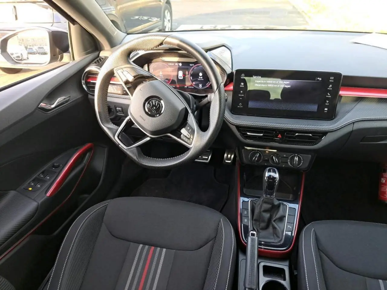 Vue intérieure côté conducteur de la Skoda Fabia Monte Carlo 2024 avec volant sport cuir et inserts rouges décoratifs.