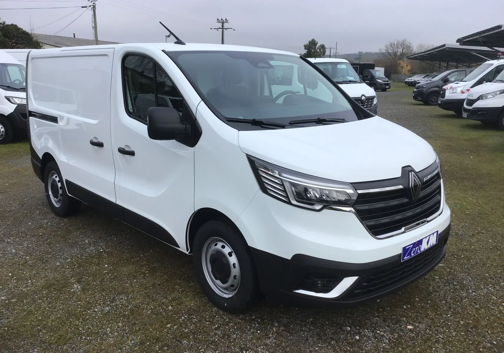 Vue 3/4 avant droit d’un fourgon Renault Trafic blanc 2025 avec calandre noire et feux LED distinctifs.