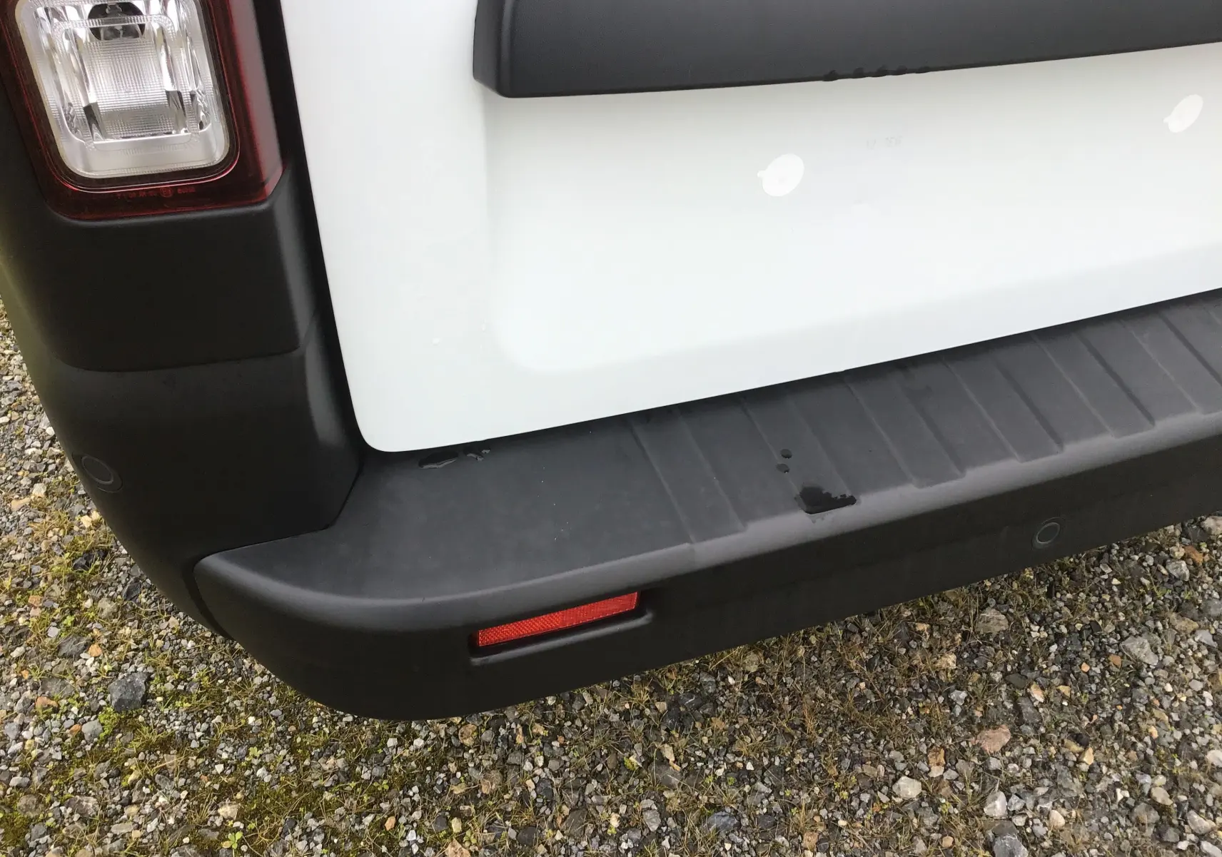Gros plan sur le coin arrière gauche blanc du Renault Trafic Fourgon 2025, avec feu arrière et pare-chocs noir texturé.