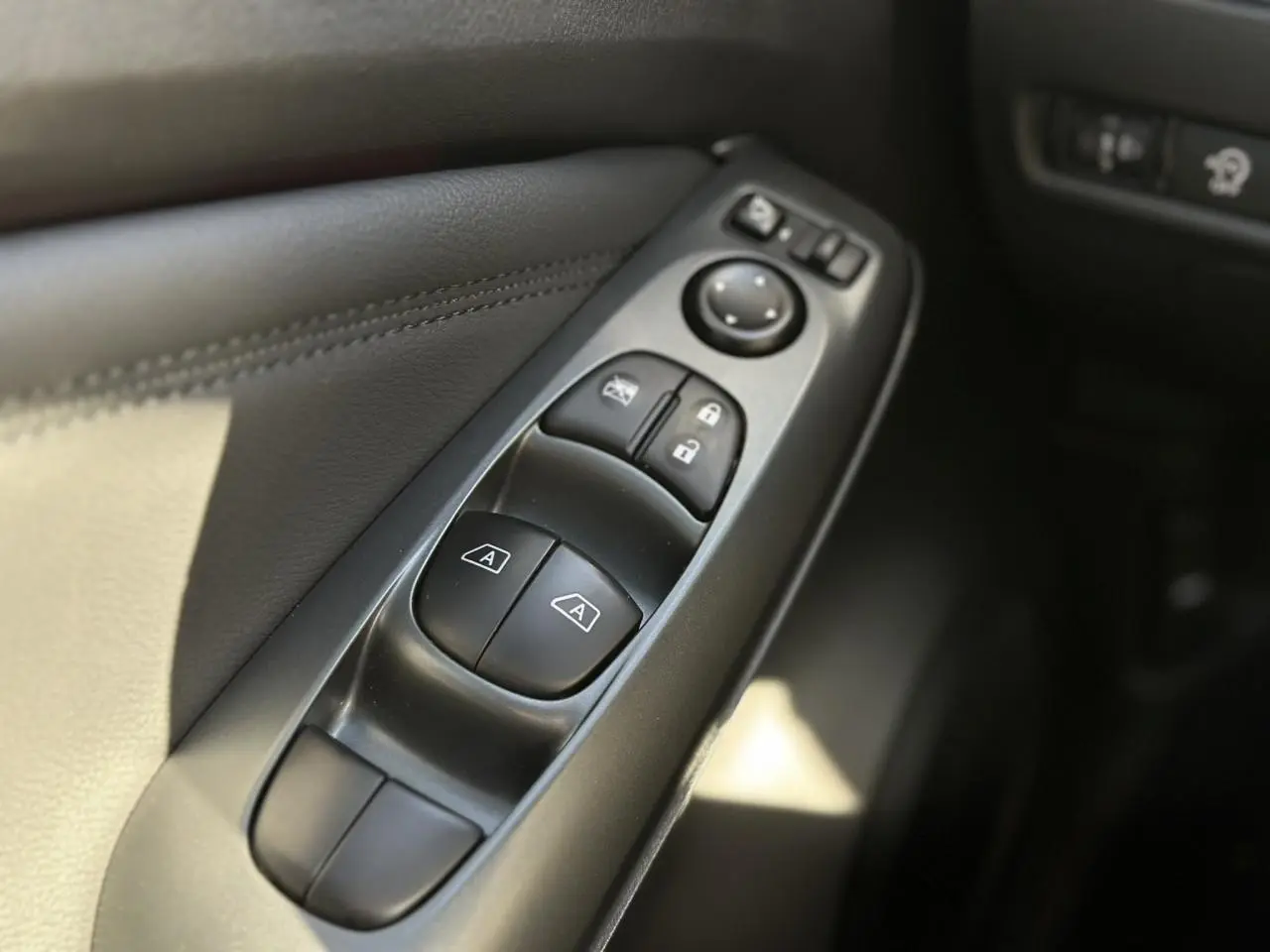 Gros plan sur les commandes des vitres et rétroviseurs côté conducteur du Nissan Juke noir 2025.