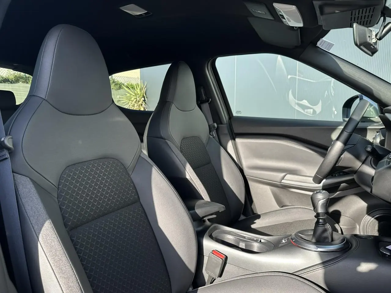 Vue intérieure côté droit du Nissan Juke 2025 noir, montrant les sièges avant en cuir et la console centrale avec levier de vitesses manuel.