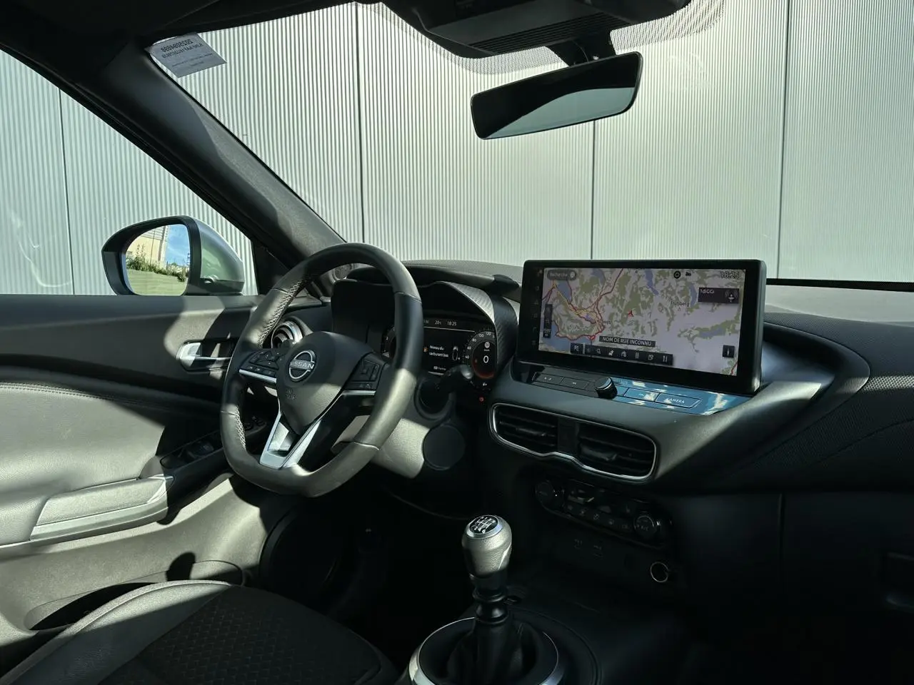 Vue intérieure côté conducteur du Nissan Juke 2025 noir, avec volant cuir, écran tactile et levier de vitesse manuel.