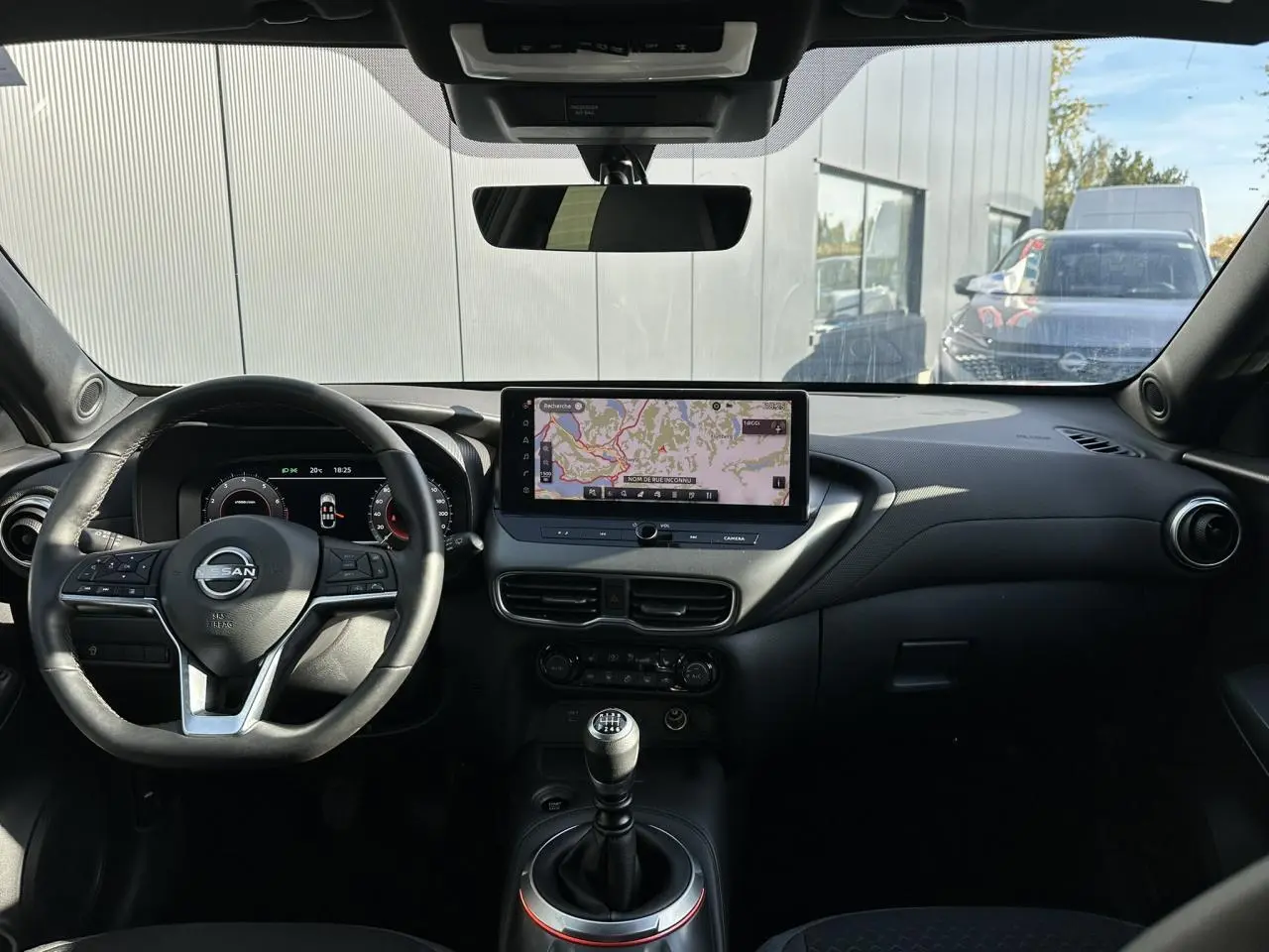 Vue intérieure avant du Nissan Juke noir 2025, mettant en valeur le volant, le combiné digital et l'écran tactile central.
