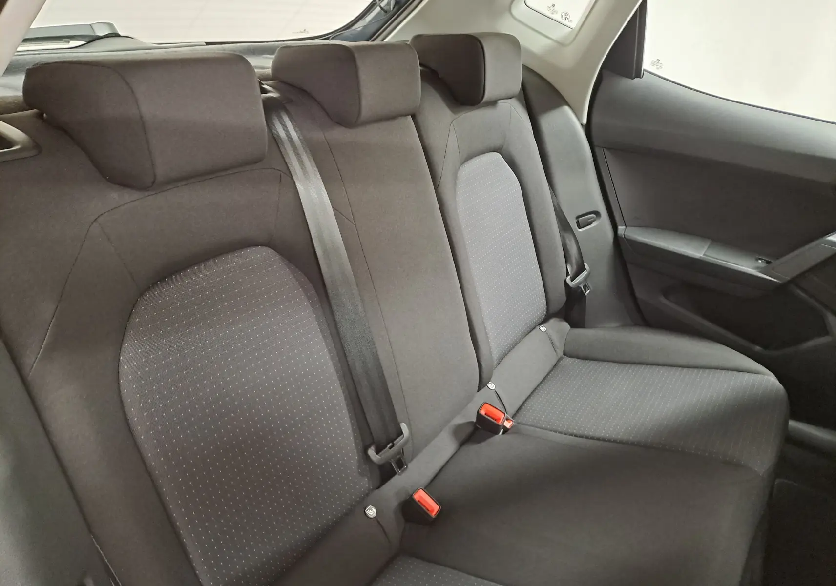 Vue intérieure de la banquette arrière du SEAT Ibiza 2025, sièges en tissu gris foncé avec ceintures de sécurité visibles.