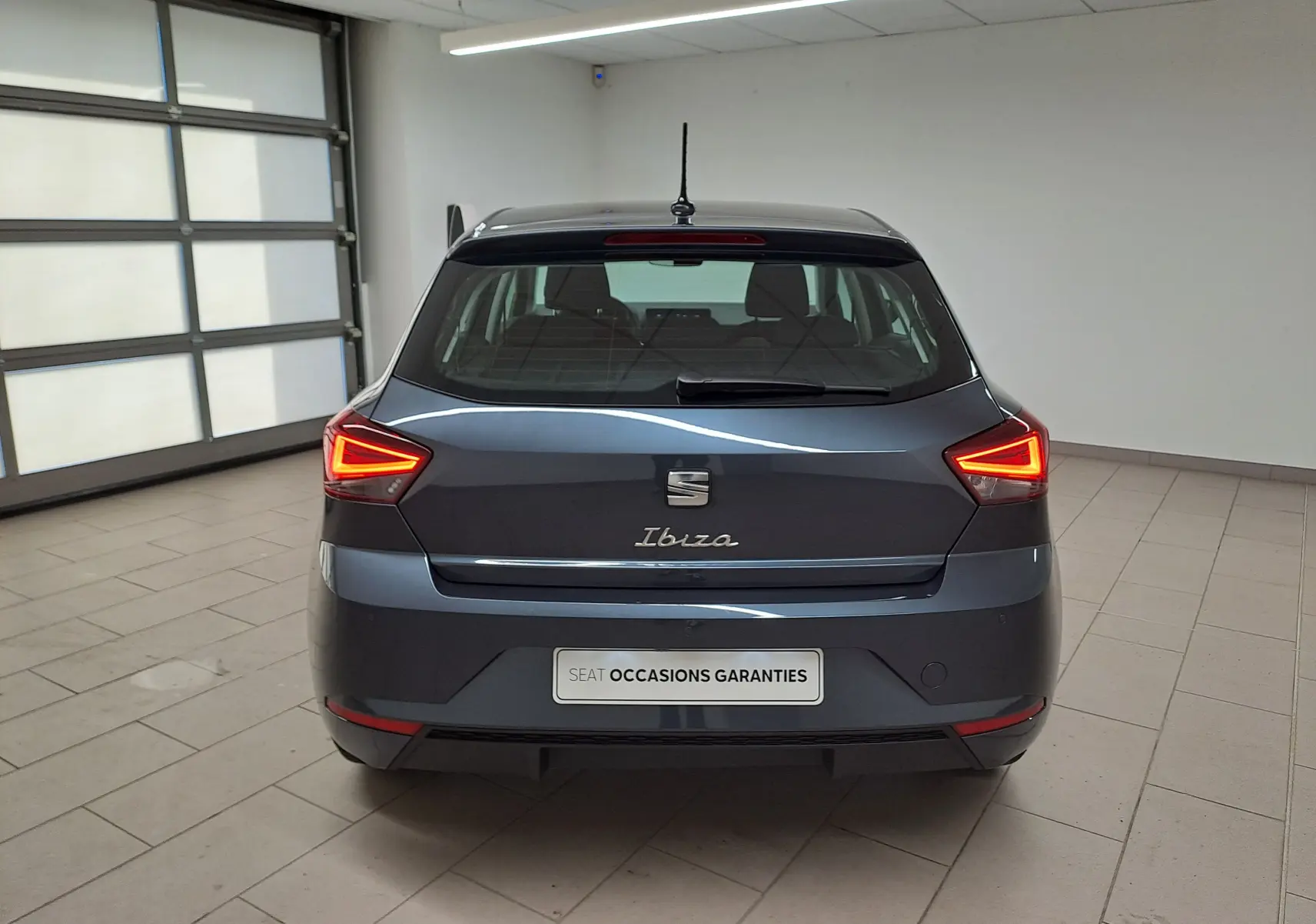 Vue arrière d'une SEAT Ibiza 2025 gris magnétique avec feux LED allumés dans un garage lumineux.