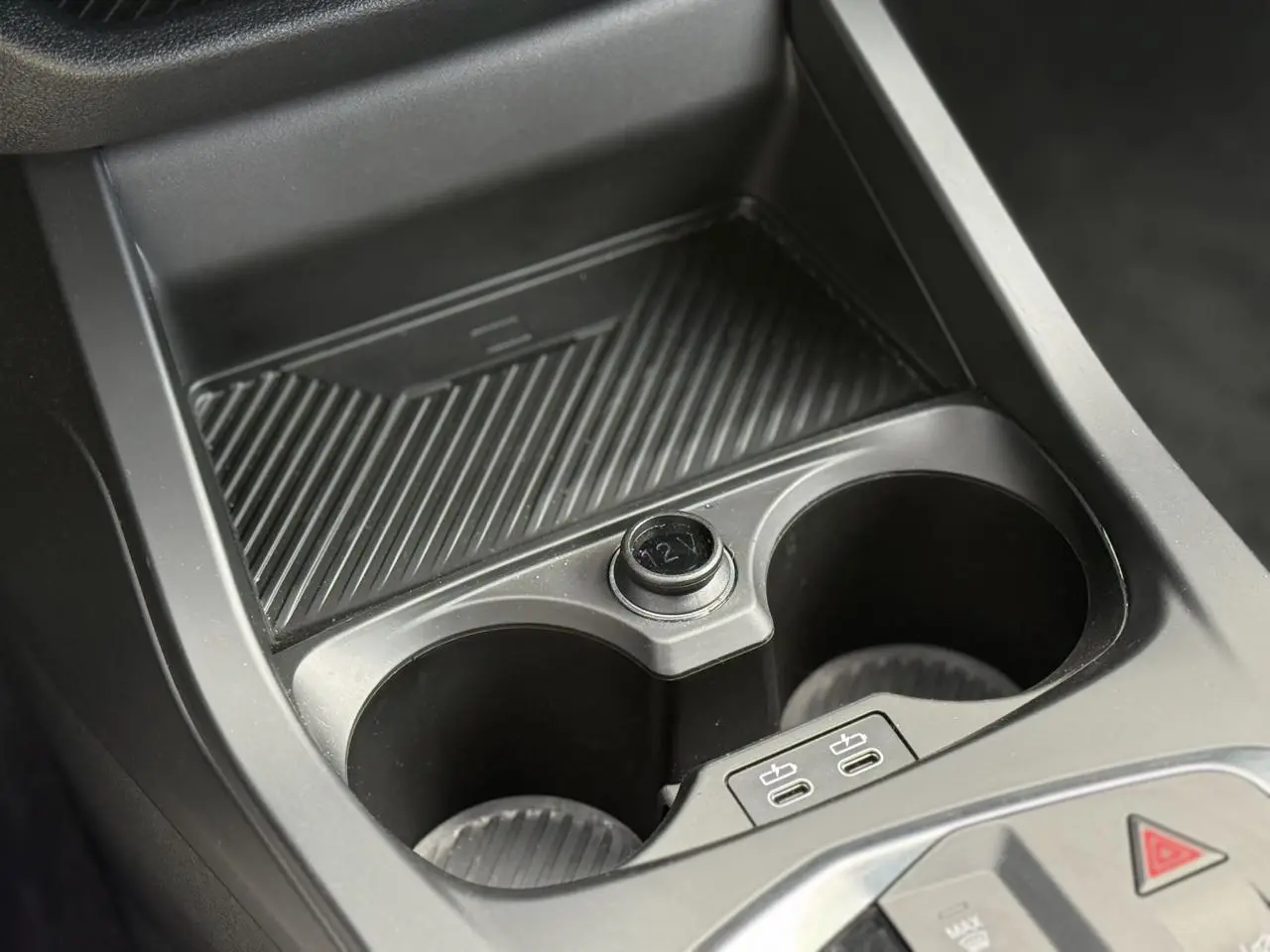 Gros plan sur la console centrale noire de la BMW Série 1 118d M Sport, avec porte-gobelets et prises USB-C visibles.