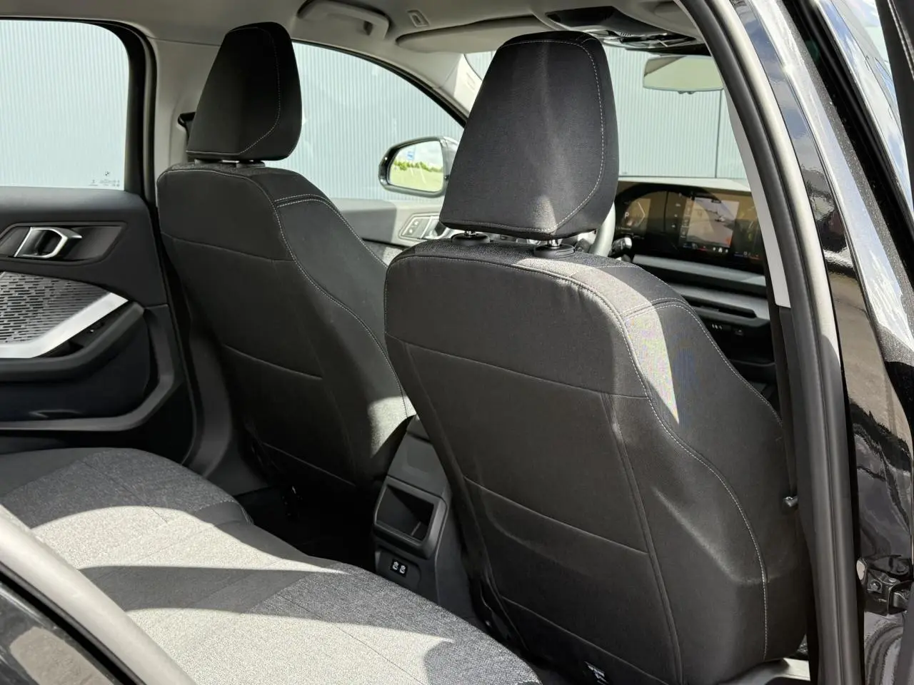 Vue intérieure arrière côté gauche de la BMW Série 1 118dA 2025 en Saphirschwarz avec sellerie tissu anthracite.