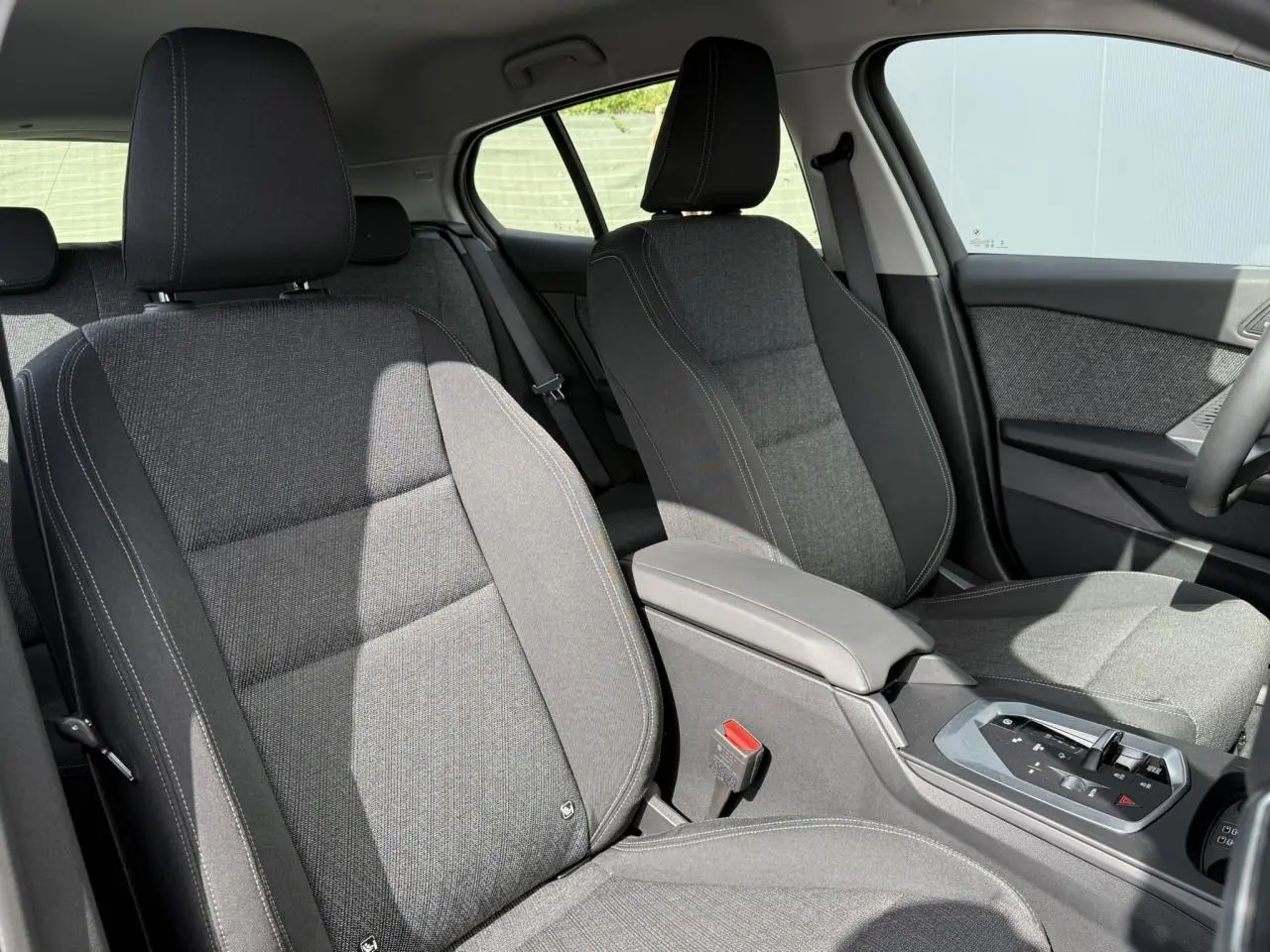 Vue intérieure côté avant droit de la BMW Série 1 118d M Sport 2025, sièges tissu anthracite avec accoudoir central.