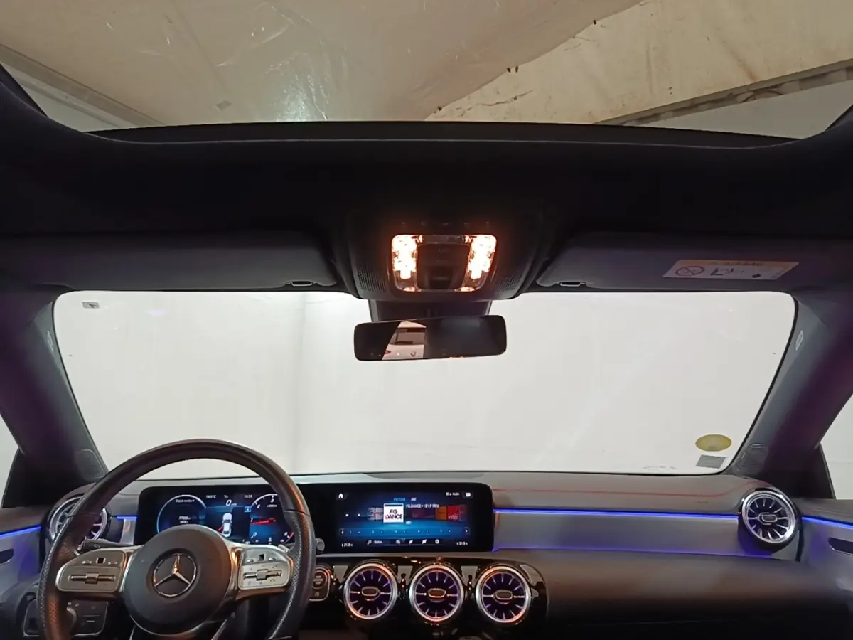 Vue intérieure avant du tableau de bord et volant cuir de la Mercedes CLA 200 d AMG Line 2022 avec éclairage d'ambiance bleu.