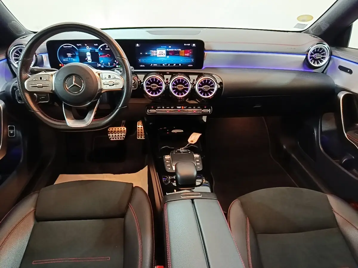 Vue intérieure avant du Mercedes CLA 200 d AMG Line 2022, tableau de bord noir avec éclairage LED violet et volant cuir.