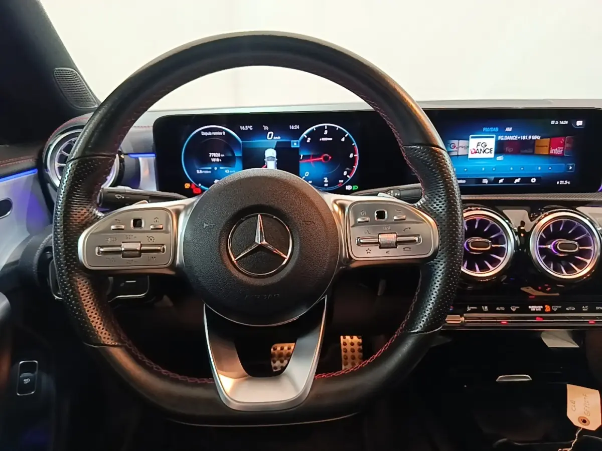 Vue frontale du volant cuir noir perforé et du tableau de bord numérique éclairé d'une Mercedes CLA 200 d AMG Line 2022.