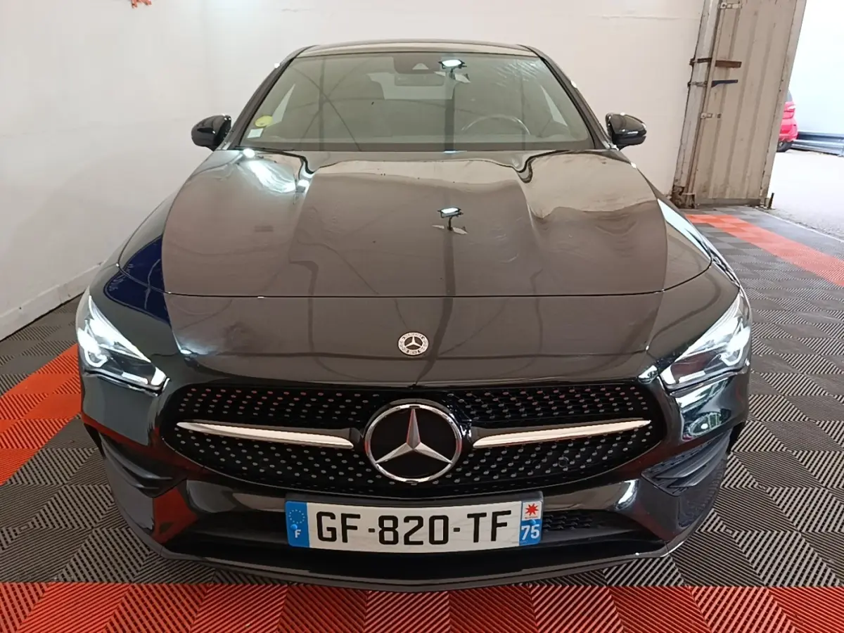 Vue de face d'une Mercedes CLA 200 d AMG Line noire avec calandre étoilée et phares LED allumés.