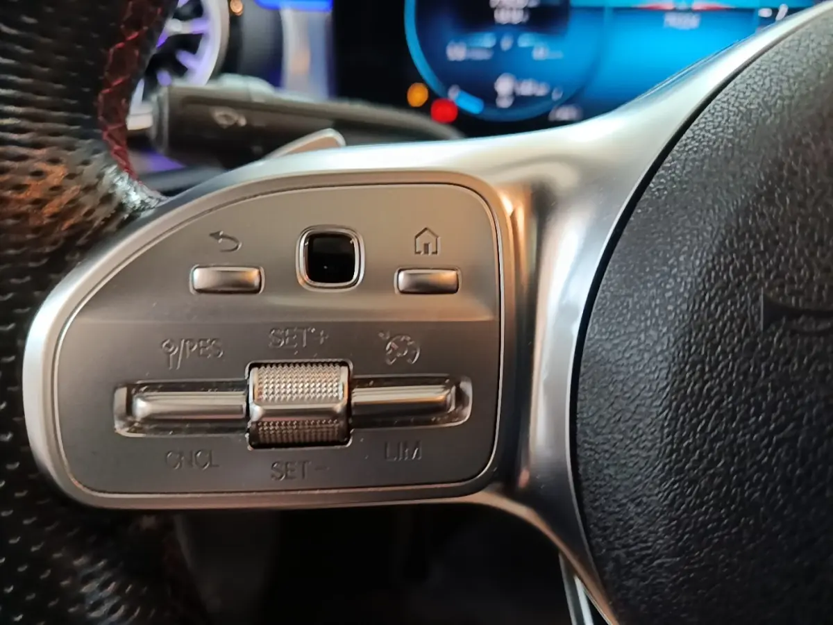 Gros plan sur les commandes du volant en cuir noir d’une Mercedes CLA 200 d AMG Line 2022, avec affichage digital bleu en arrière-plan.