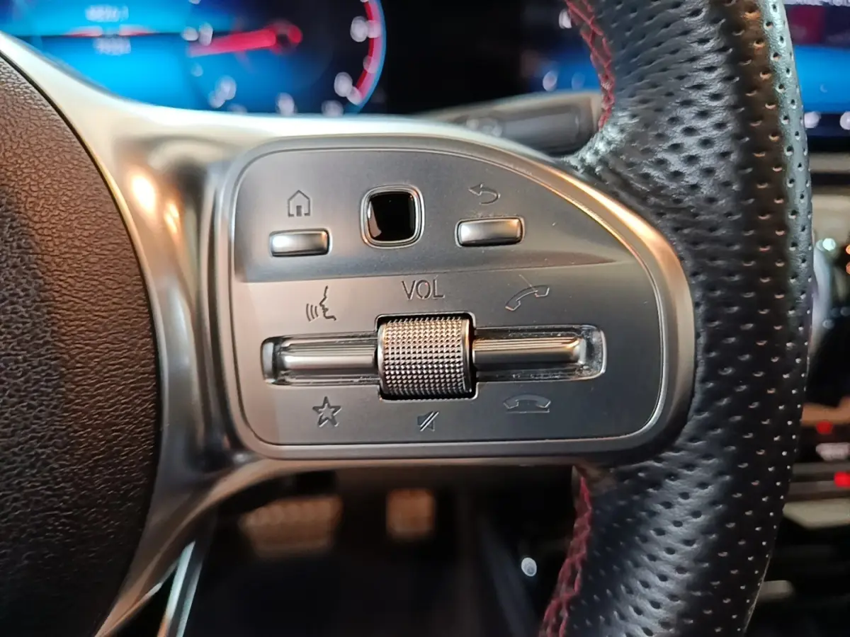 Gros plan sur les commandes argentées du volant cuir perforé noir d’une Mercedes CLA 200 d AMG Line 2022.