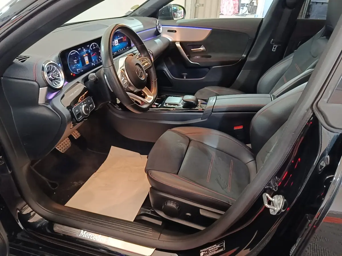 Vue intérieure côté conducteur de la Mercedes CLA 200 d AMG Line noire, avec tableau de bord digital et sièges sport noirs.