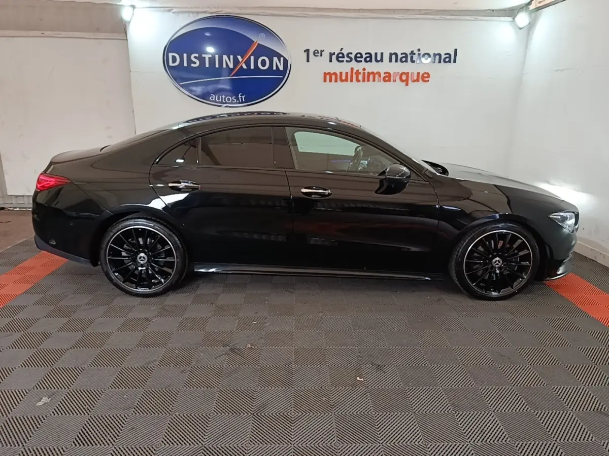 Vue de profil côté gauche d'une Mercedes CLA 200 d AMG Line noire, avec jantes noires et vitres teintées, en intérieur showroom.