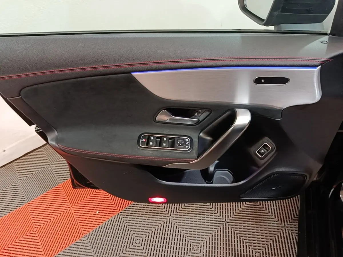 Détail de la porte côté gauche de la Mercedes CLA 200 d AMG Line noire, avec garniture noire, surpiqûres rouges et insert aluminium.