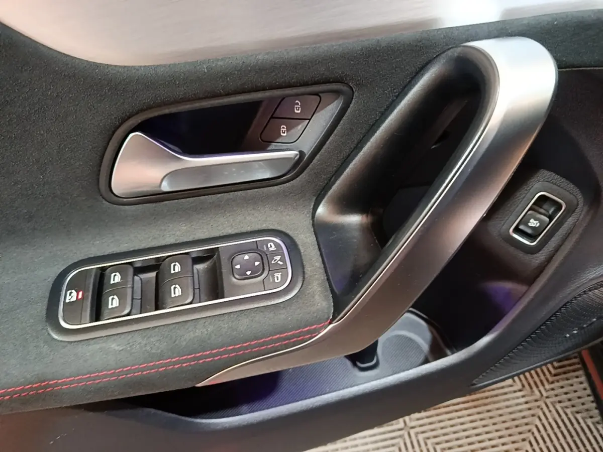 Gros plan sur la porte côté gauche d'une Mercedes CLA 200 d AMG Line noire, avec commandes de vitres et poignée alu.