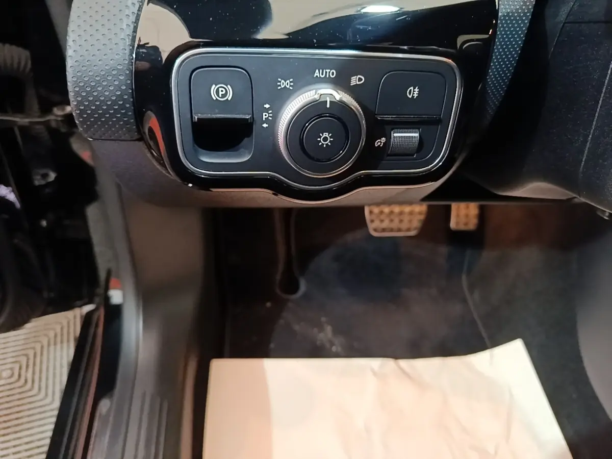 Gros plan sur les commandes d’éclairage et frein à main électrique dans l’habitacle noir d’une Mercedes CLA 200 d AMG Line 2022.