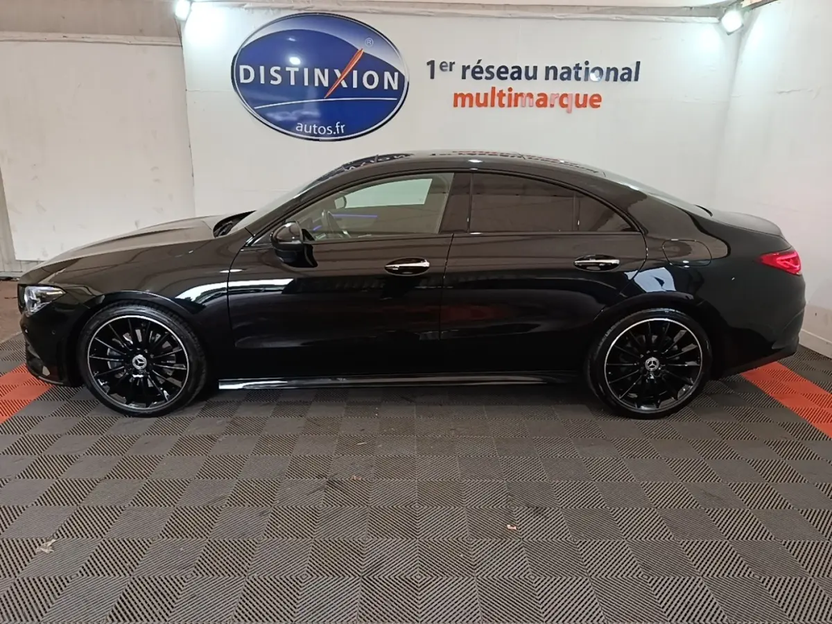 Vue de profil côté gauche d'une Mercedes CLA 200 d AMG Line noire avec jantes noires brillantes en intérieur showroom.