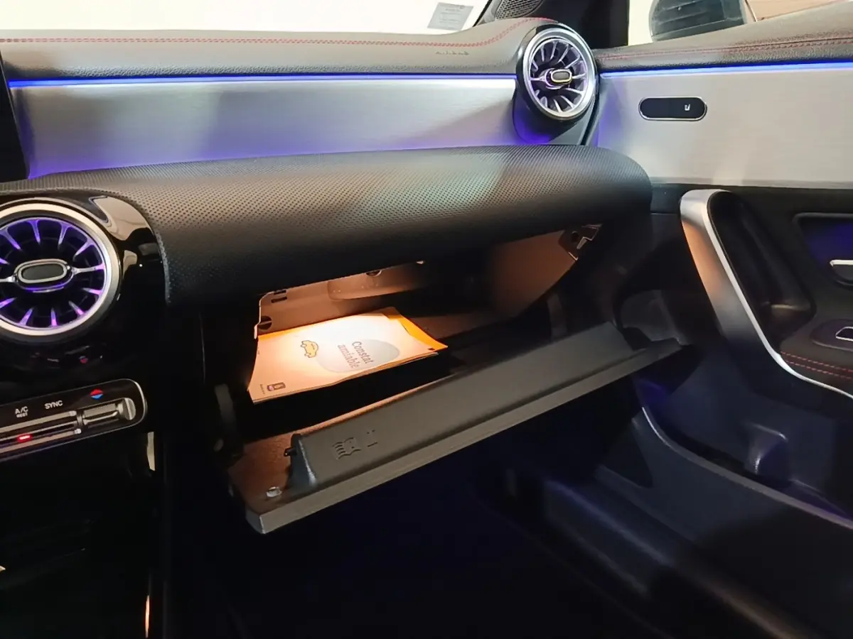 Vue intérieure côté passager de la Mercedes CLA 200 d AMG Line 2022, boîte à gants ouverte avec éclairage d'ambiance violet.