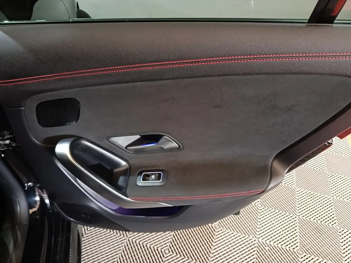 Gros plan sur la porte intérieure côté gauche noire avec surpiqûres rouges et poignée alu de la Mercedes CLA 200 d AMG Line.