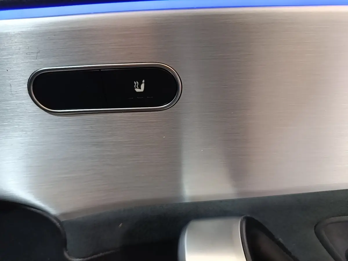 Gros plan sur le bouton de siège chauffant sur la garniture intérieure en aluminium brossé d’une Mercedes CLA 200 d AMG Line noire.