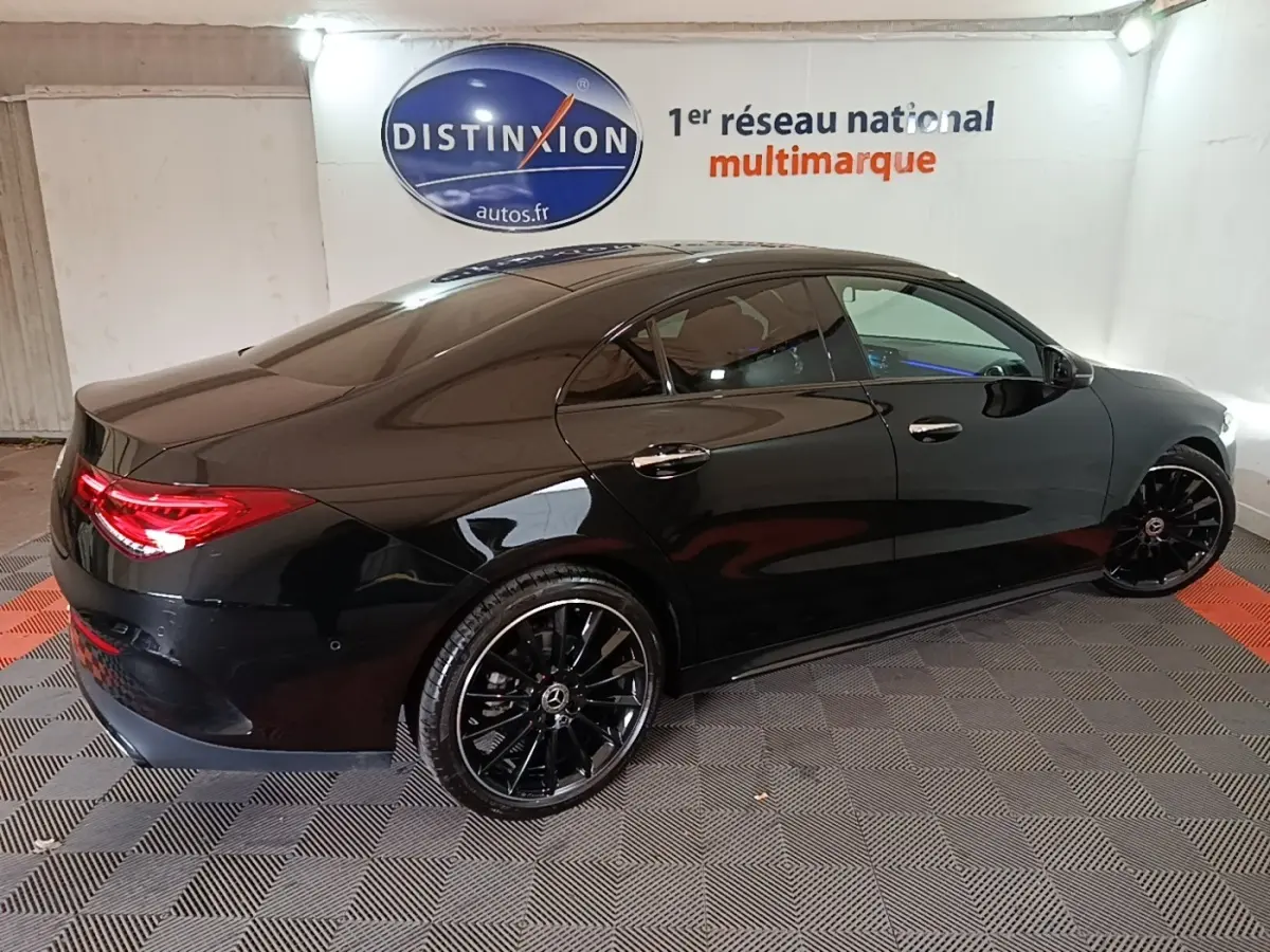 Vue 3/4 arrière droite d'une Mercedes CLA 200 d AMG Line noire avec jantes noires et feux arrière LED allumés.