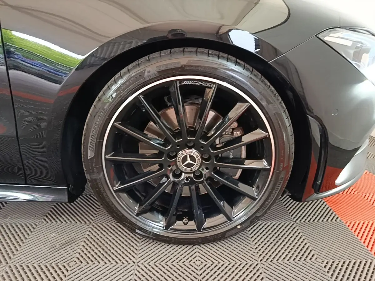Gros plan sur la roue avant gauche noire AMG avec jante multibranches et logo Mercedes visible sur une Mercedes CLA 200 d AMG Line.