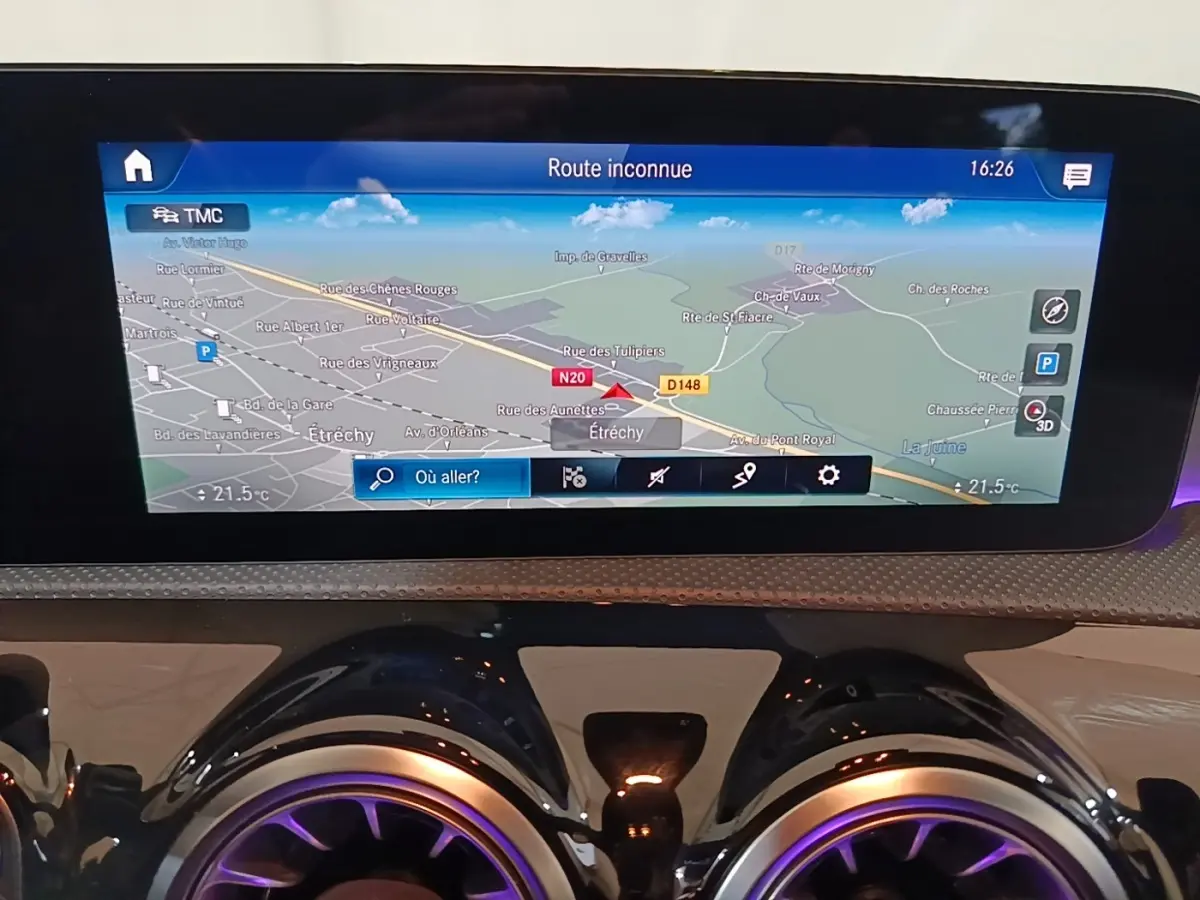 Gros plan sur l'écran tactile de navigation 10,3 pouces et les aérateurs ronds à éclairage violet du tableau de bord d'une Mercedes CLA 200 d AMG Line noire.