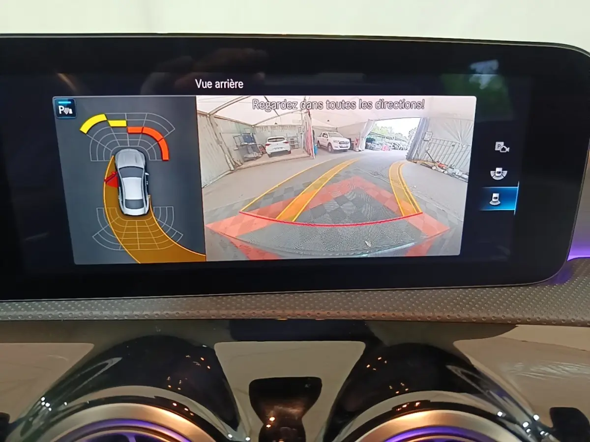 Écran tactile intérieur montrant la caméra de recul et l'aide au stationnement du Mercedes CLA 200 d AMG Line noir.