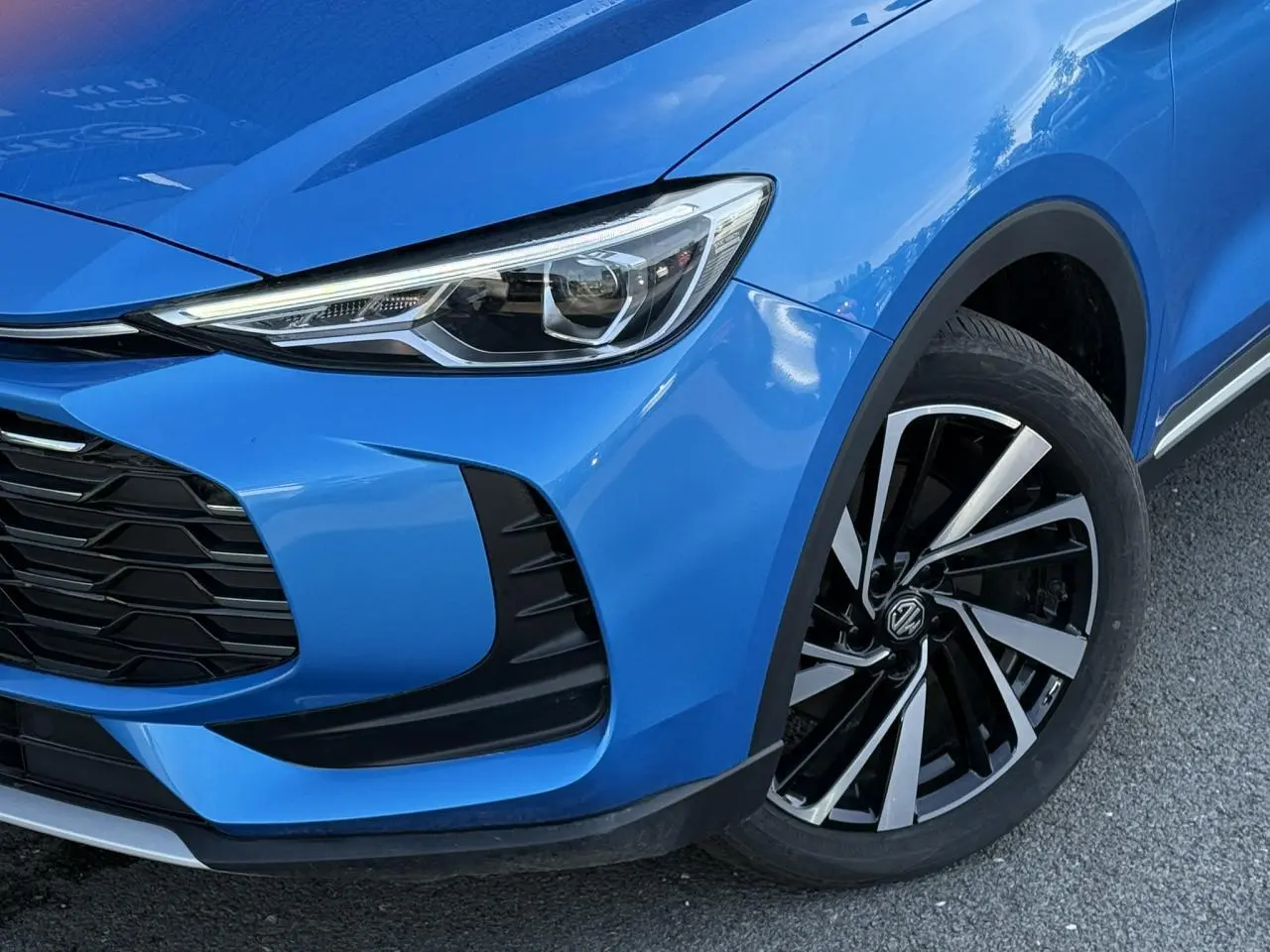 Gros plan sur l'avant droit bleu Como du MG ZS 1.5 Hybrid+ 197 Luxury, avec phares LED et jantes alliage noires et argentées.