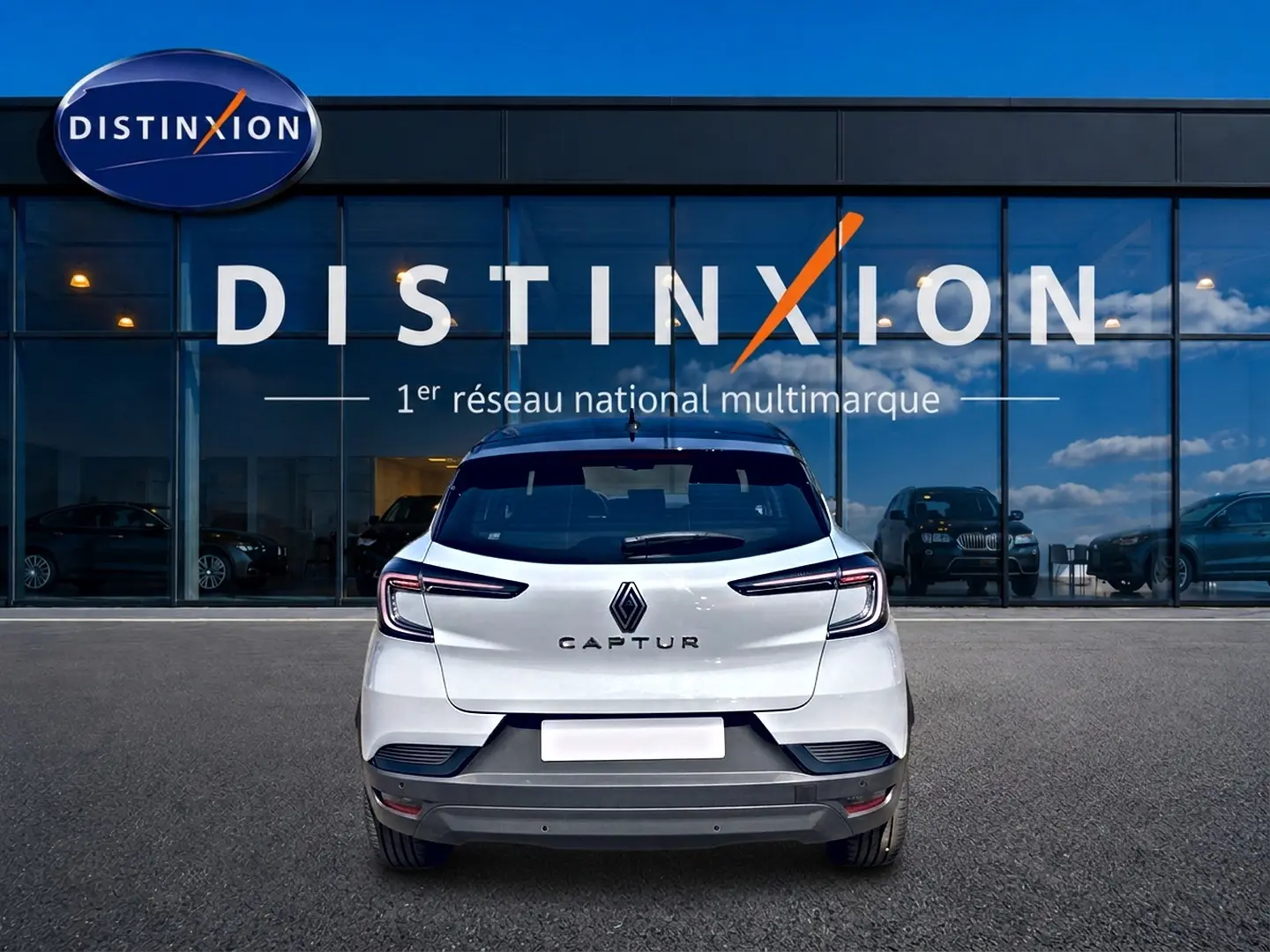 Vue arrière d'un Renault Captur 1.2 TCe 115 Techno blanc avec toit noir, garé devant une vitrine Distinxion.