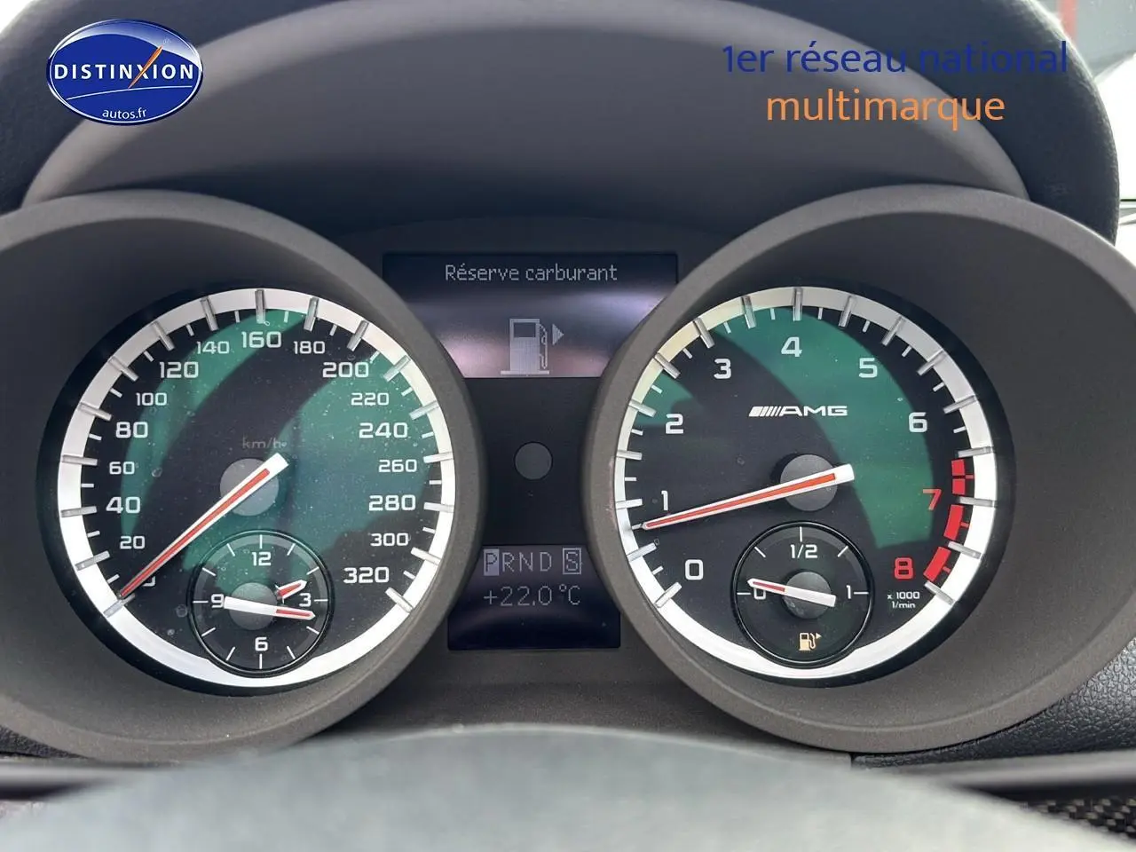 Gros plan sur le tableau de bord noir du Mercedes SLK 55 AMG 7G-Tronic, affichant le compteur et l'alerte réserve carburant.