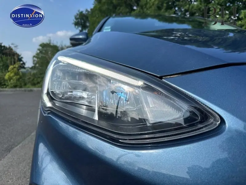 Gros plan sur le phare avant droit d'une Ford Focus bleu azur métallisé, soulignant les détails du bloc optique moderne.